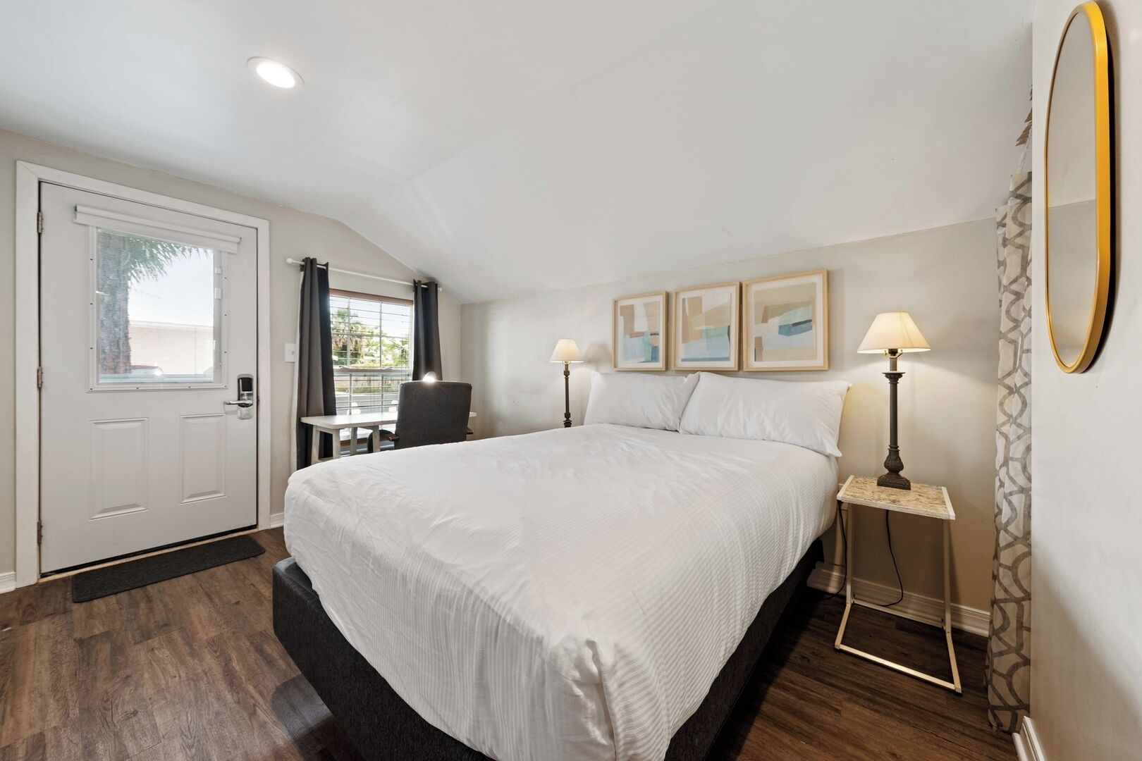 A hotel room with a large bed, a desk, two bedside lamps, and a mirror on the wall.