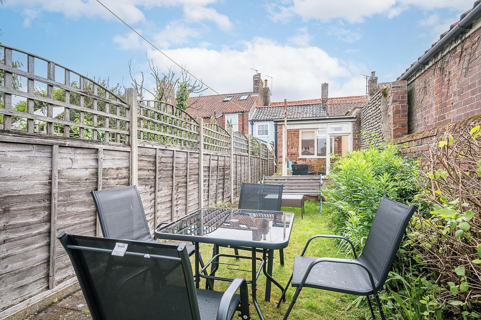 A patio with a table and chairs, a wooden fence, and a brick house in the background.