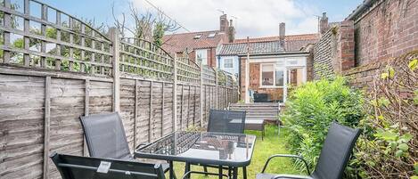 A patio with a table and chairs, a wooden fence, and a brick house in the background.