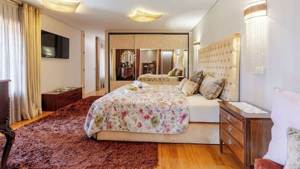 Ein Schlafzimmer mit einem großen Bett, einer Holzkommode, einem Spiegel und einem Fernseher an der Wand.