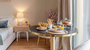 Ein gemütliches Hotelzimmer mit schön gedecktem Frühstückstisch, einer Nachttischlampe und Blick auf den Strand durch das Fenster.