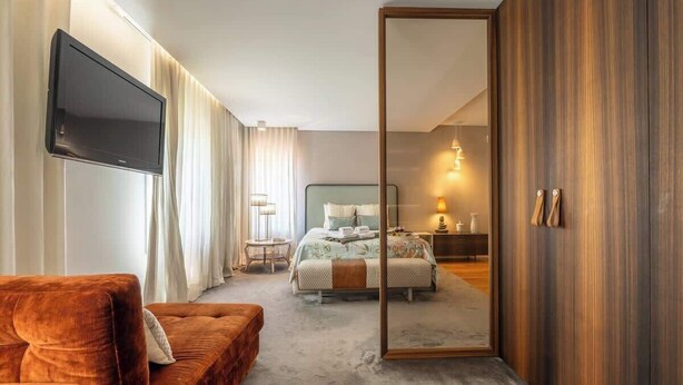 A modern hotel room with a large bed, a sofa, a TV, and a sliding door leading to a bathroom. - HostWise - Modern Comfort & Shared Pool in Paredes (Vandoma)