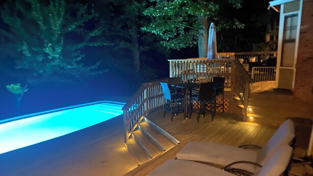 Una terraza de madera con piscina, sillas de descanso y una mesa con sillas.