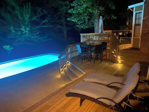 Una terraza de madera con piscina, sillas de descanso y una mesa con sillas.