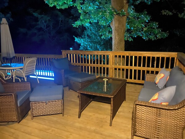 Terraza al aire libre con mobiliario de mimbre, incluyendo sillas y una mesa, y barandilla de madera.