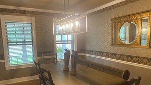Comedor con mesa de madera, sillas, lámpara de araña, espejo grande y ventana con persianas.