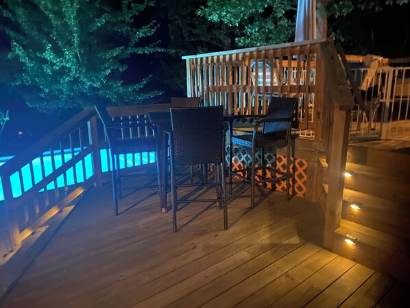 Terraza de madera con mobiliario exterior, barandilla y escalera que sube a un nivel superior.