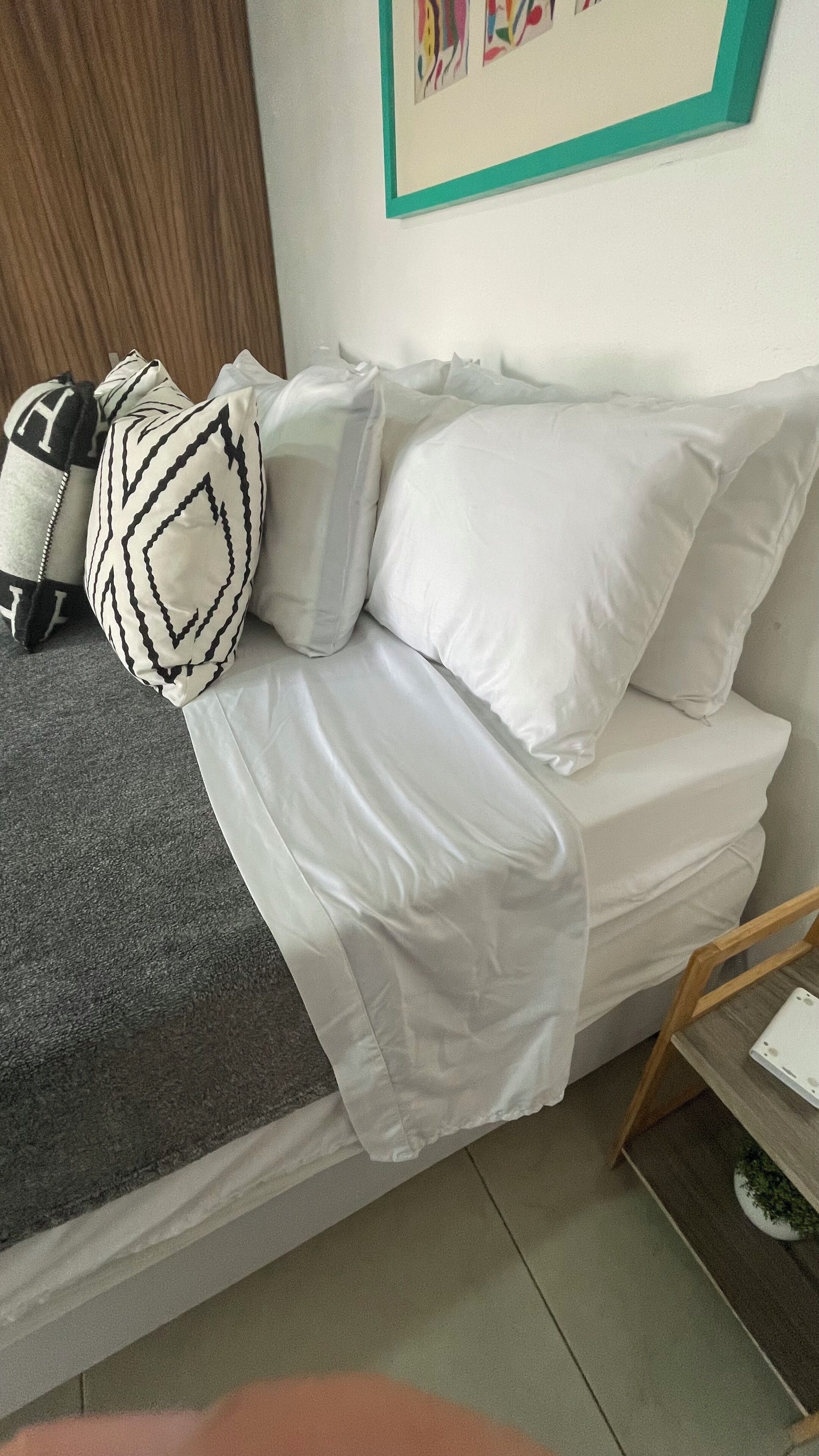 Una cama bien hecha con sábanas blancas, una almohada estampada y una manta gris.
