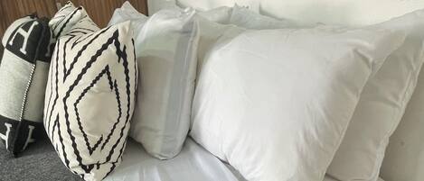 Una cama bien hecha con sábanas blancas, una almohada estampada y una manta gris.