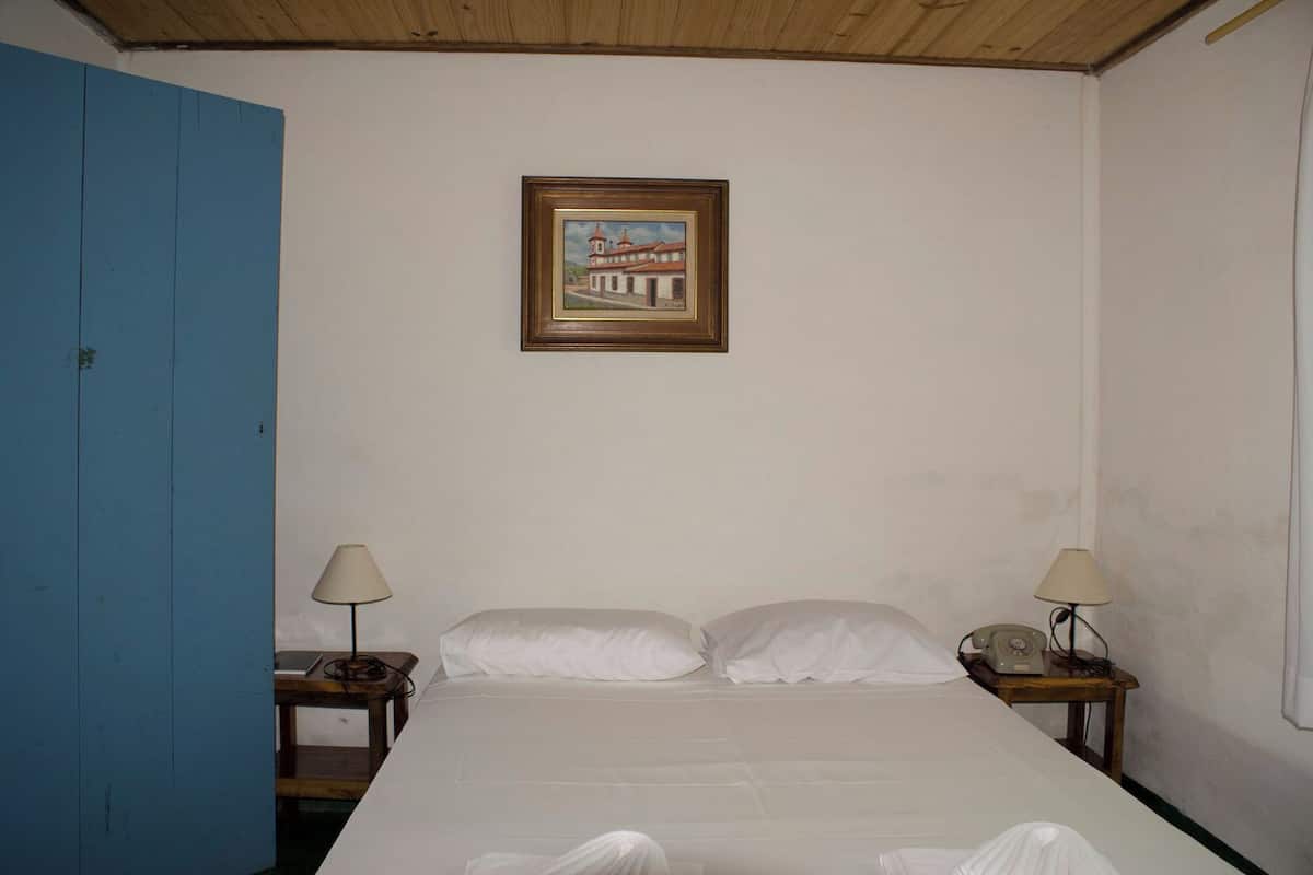 Un dormitorio con una cama, dos mesitas de noche, una lámpara en cada una, un cuadro enmarcado en la pared y una puerta azul.