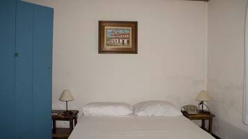 Un dormitorio con una cama, dos mesitas de noche, una lámpara en cada una, un cuadro enmarcado en la pared y una puerta azul.
