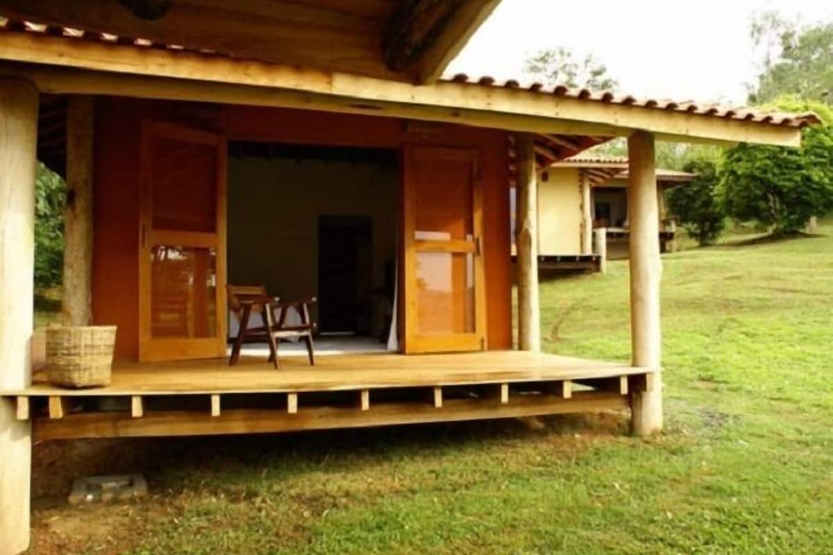 Una estructura de madera con puerta abierta, un banco y una cesta en el porche.