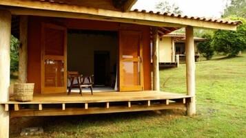 Una estructura de madera con puerta abierta, un banco y una cesta en el porche.