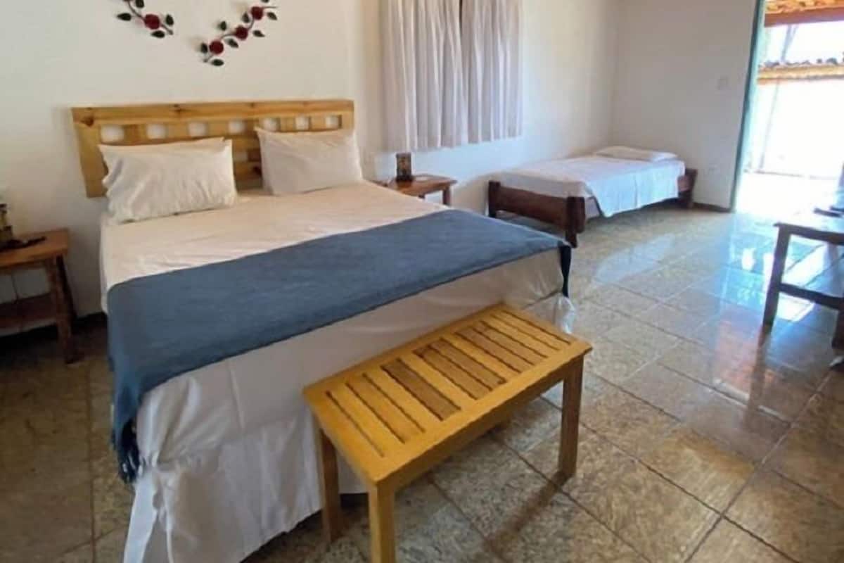 Un dormitorio con cama, una banca, una mesita de noche y una ventana con cortinas.