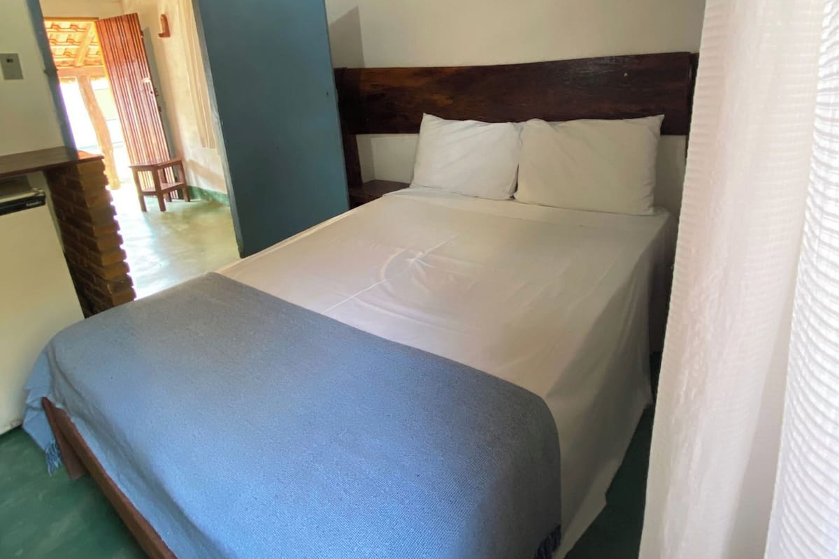 Una cama bien tendida con una manta azul, cabecera de madera y almohadas blancas.