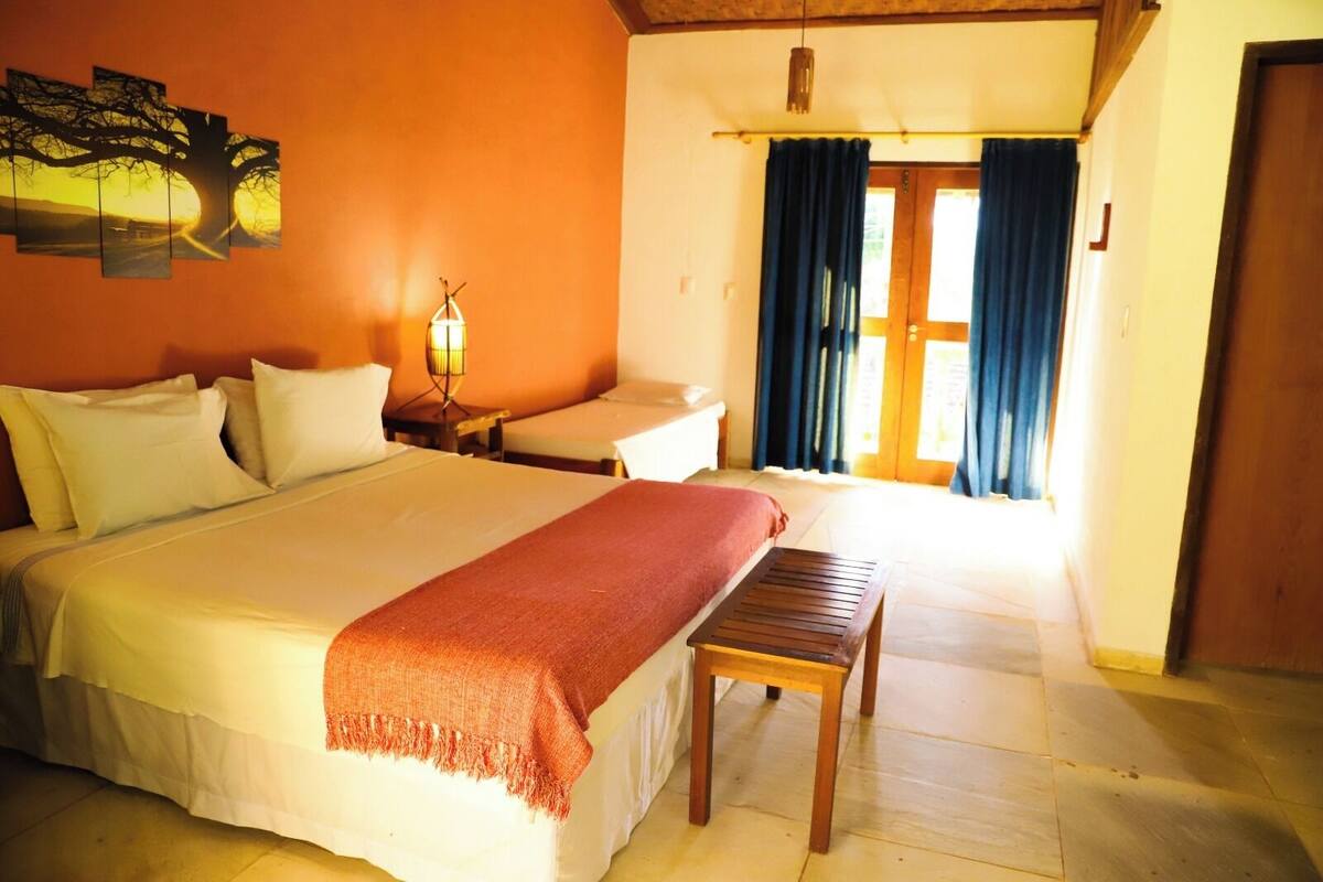 Una habitación de hotel con una cama grande, un banco, una mesita de noche y una lámpara.