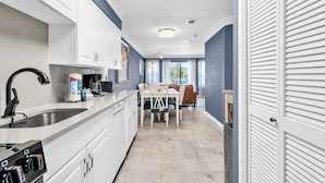 A modern kitchen with white cabinets, a stainless steel sink, and a dining area with a table and chairs. - Poolside Villas 104 near beach sleeps 5 (Destin)