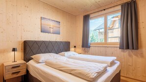 Ein Zimmer mit Holzwänden, einem Bett, einem Nachttisch, einer Lampe und einem Fenster mit Vorhängen.