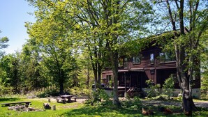Ein rustikales Blockhaus mit einer Terrasse, umgeben von üppigem Grün und Bäumen.