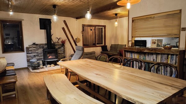 A cozy living room with a wooden table, benches, a fireplace, and a bookshelf. - Quiet Forest Retreat with Views of Mt. Yotei – 3 Bedrooms, 10 Minutes from Niseko Resort (ニセコ町)