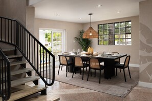Un coin repas avec une table noire, des chaises et un luminaire suspendu. Un escalier est visible sur la gauche.