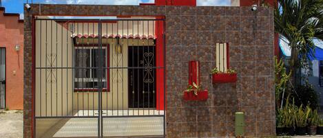 Una casa con entrada protegida por un portón, fachada de piedra y un pequeño jardín con plantas en macetas.