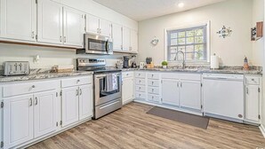 Una cocina con armarios blancos, electrodomésticos de acero inoxidable y piso de madera.