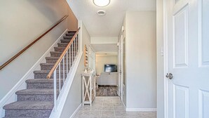 Interior de una casa con una escalera, una puerta y un pasillo que conduce a una sala de estar.