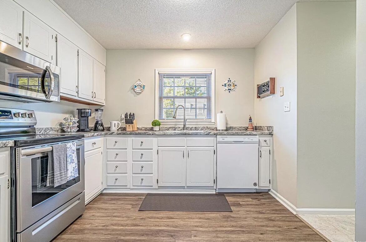 A modern kitchen with white cabinets, a stainless steel oven, a built-in microwave, and a granite countertop.