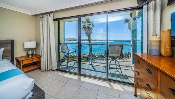 Ein Hotelzimmer mit Balkon, einem Bett, einem Nachttisch, einer Kommode und Blick aufs Meer.