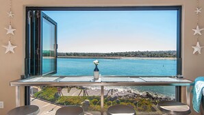A room with a large window overlooking a body of water, a small table with a vase, and two chairs.
