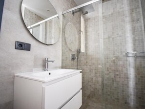 A modern bathroom with a white vanity, a round mirror, and a glass-enclosed shower. - Luxury Villa Facing the Sea in Cotobro (Almuñecar)