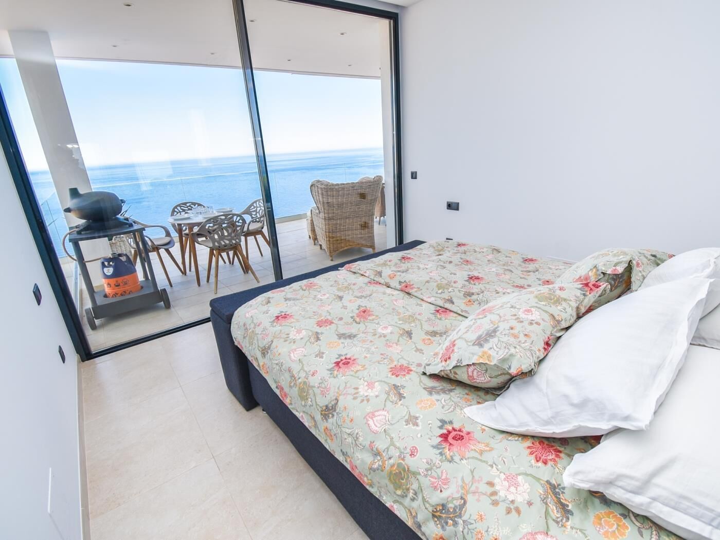 A bedroom with a bed, a view of the sea, a dining area with chairs, and a table.