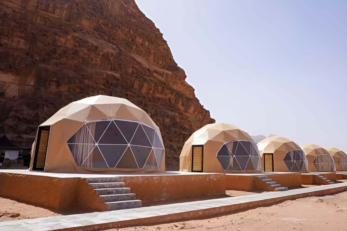 A row of dome-shaped tents with large windows, set against a rocky cliff backdrop.