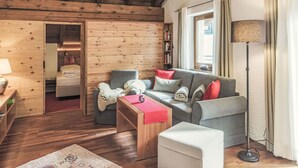 A cozy living room with wooden walls and a ceiling, a grey sofa with red cushions, a wooden coffee table, and a floor lamp. - Waldblick by Interhome (Seefeld in Tirol)