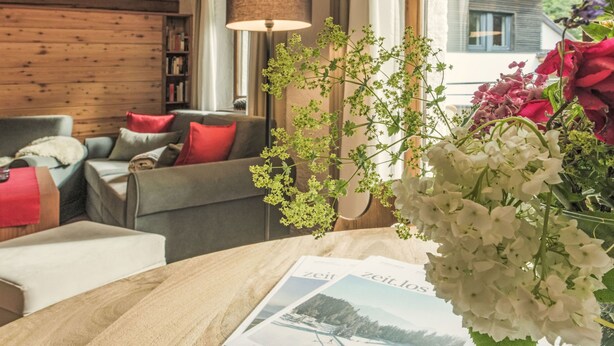 A cozy living room with a wooden ceiling, a sofa with red cushions, a table with a magazine, and a vase with flowers. - Waldblick by Interhome (Seefeld in Tirol)
