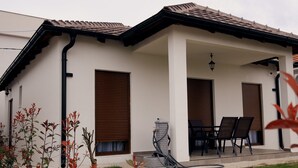 Un edificio moderno con un patio cubierto, que incluye una mesa y sillas, y una manguera conectada al edificio.