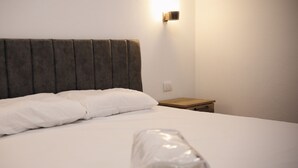 Una cama bien hecha con sábanas blancas y cabecera gris.