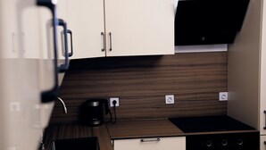 Una cocina compacta con protector contra salpicaduras de madera, una cafetera y una campana extractora negra.