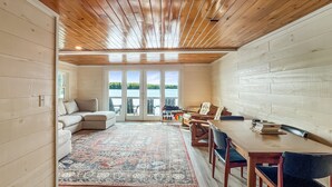 A cozy room with a wooden ceiling, a large window, a sofa, a dining table with chairs, and a patterned rug. - The Crooked Nook (Direct Lake Access) (Rockwood)