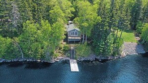 An aerial view of a house surrounded by dense forest, connected to a body of water via a dock. - The Crooked Nook (Direct Lake Access) (Rockwood)
