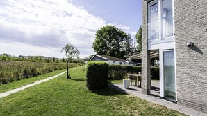 Ein modernes Haus mit Naturstein-Fassade, überdachter Terrasse und gepflegtem Rasen.