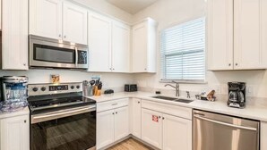 A compact kitchen with white cabinets, a stainless steel microwave, a stove, a sink, and a dishwasher.