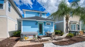 A two-story house with a blue exterior, a front porch with a table and chairs, and a palm tree in the yard.