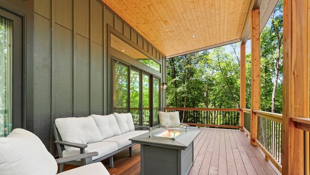 Un espace extérieur aménagé, partiellement abrité, avec un foyer intégré, une terrasse en bois et une vue sur les arbres environnants.