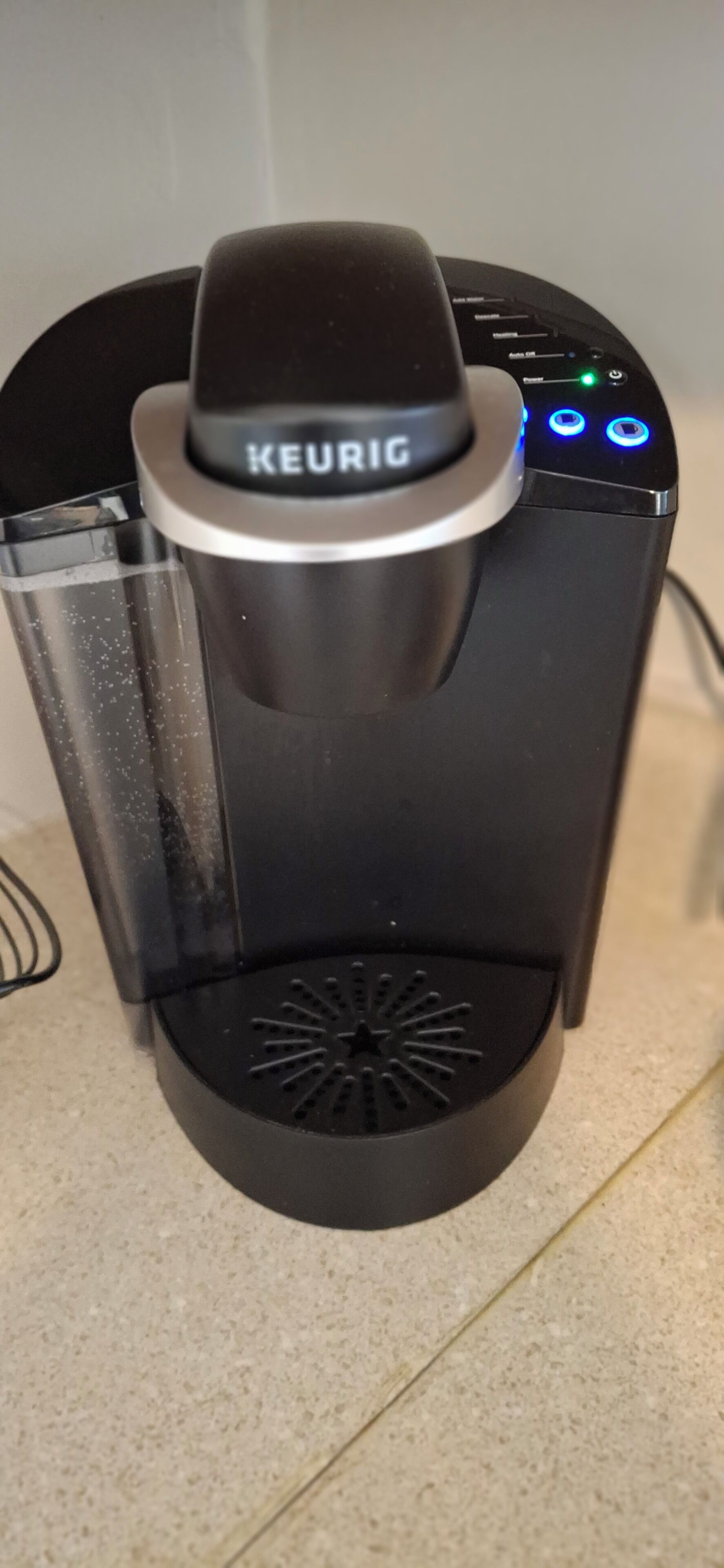 A black Keurig coffee maker with a clear water reservoir and a circular base.