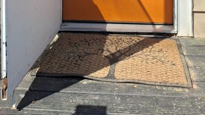 Uma porta de entrada com uma grinalda azul, uma janela com persianas e um interfone.
