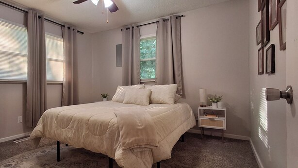 Quarto com cama, cortinas, mesa de cabeceira, luminária na parede e janela com persianas.