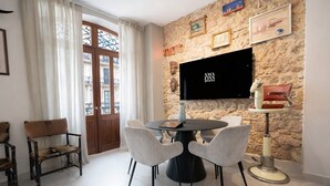Comedor con una mesa redonda, cuatro sillas, una pared de piedra con obras de arte, un televisor y un lavamanos de estilo vintage.