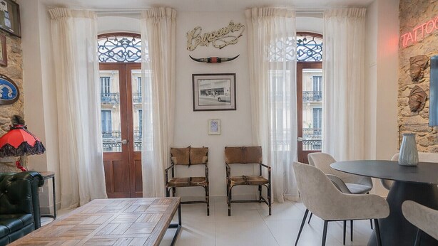 Un comedor con una mesa de madera, dos sillas, una mesa redonda con sillas, una lámpara roja y un letrero en la pared.